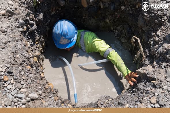 Trabajador municipal con casco azul repara una fuga de agua en una zanja inundada en Tuxpan