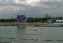 Competencia de canotaje de velocidad en una pista acuática, con atletas remando en kayaks individuales.