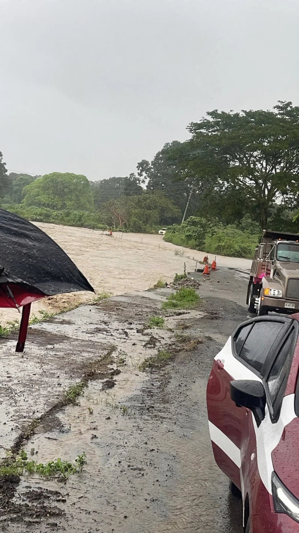 Carretera inundada por el agua del río; conos naranjas y vehículos detenidos