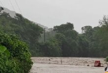 Río desbordado inunda el camino; un auto blanco se detiene al borde del agua