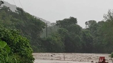 Río desbordado inunda el camino; un auto blanco se detiene al borde del agua
