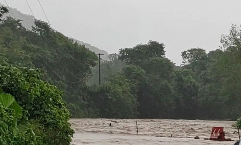 Río desbordado inunda el camino; un auto blanco se detiene al borde del agua