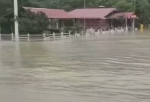 Agua turbia cubre el terreno junto a un Oxxo en la carretera federal 127, con la sierra al fondo