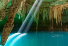 Interior de un cenote con agua turquesa y un rayo de luz