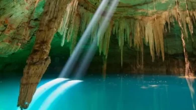 Interior de un cenote con agua turquesa y un rayo de luz
