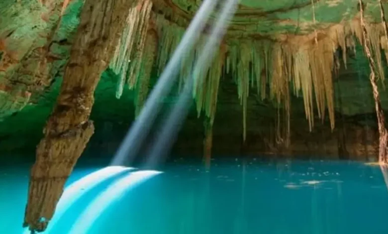 Interior de un cenote con agua turquesa y un rayo de luz