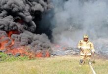 Bombero con manguera frente a llantas en llamas y columna de humo negro en el Libramiento Portuario de Tuxpan