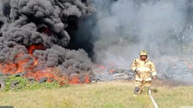 Bombero con manguera frente a llantas en llamas y columna de humo negro en el Libramiento Portuario de Tuxpan