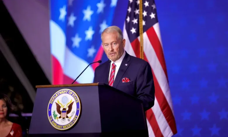 El embajador de Estados Unidos en México, Ronald Johnson, durante un mensaje desde el podio de la Embajada estadounidense en la Ciudad de México, con banderas de su país al fondo.