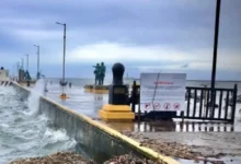 Olas rompen contra el malecón bajo cielo nublado; Protección Civil mantiene la Alerta Gris