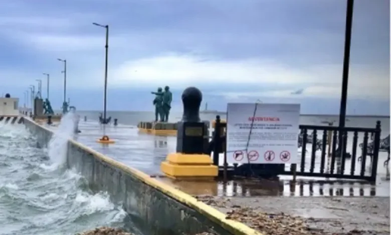 Olas rompen contra el malecón bajo cielo nublado; Protección Civil mantiene la Alerta Gris