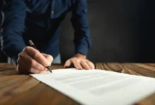 Mano firmando un documento con pluma sobre un escritorio de madera