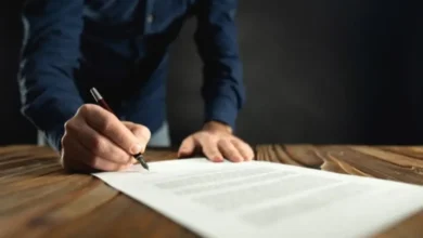Mano firmando un documento con pluma sobre un escritorio de madera
